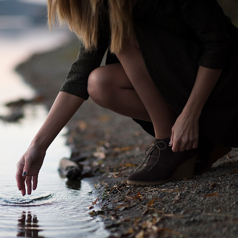 frau hockt am ufer eines sees und taucht eine hand ins wasser